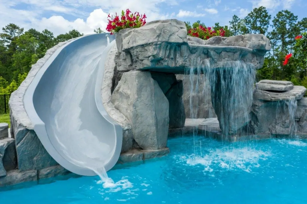 Resort-style pool with waterfall and slide in a lush backyard